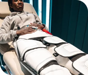 A woman reclined on a treatment bed wearing a leg compressor garment and pulse oximeter