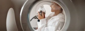 Woman wearing a white robe smiles as she applied a breathing mask inside a hyperbaric oxygen therapy chamber
