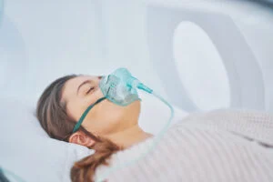 Woman wearing a breathing mask while lying inside a hyperbaric oxygen therapy chamber in a medical setting